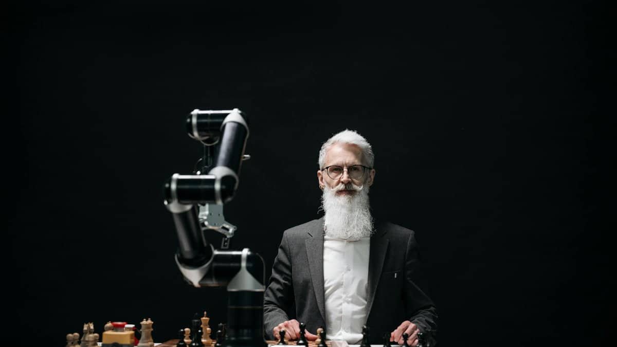 A bearded man in suit playing chess with robotic arm, showcasing AI strategy.