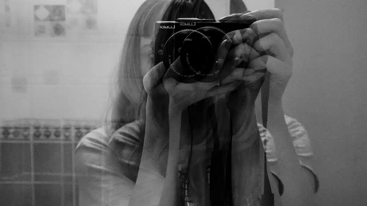 Black and white double exposure of a woman holding a camera, creating a layered visual effect.