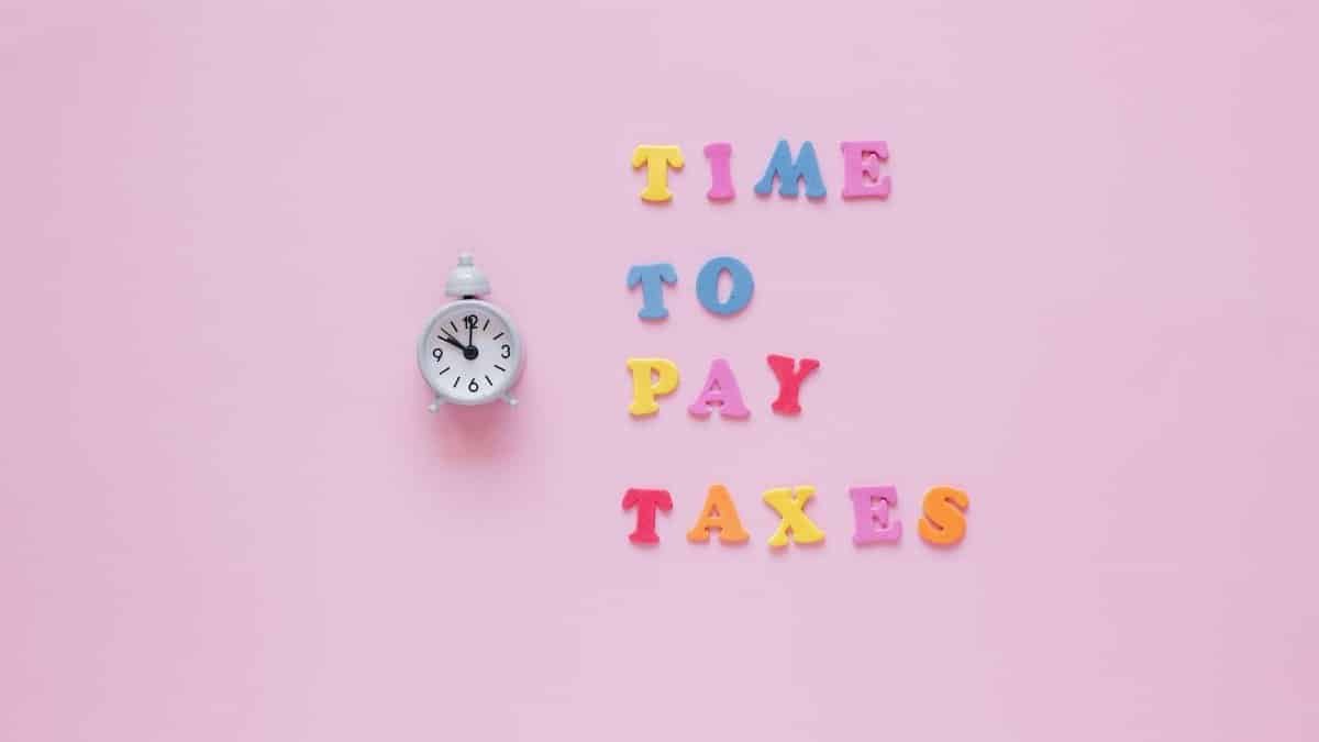 Colorful letters spell 'Time to Pay Taxes' next to a clock on a pink surface.