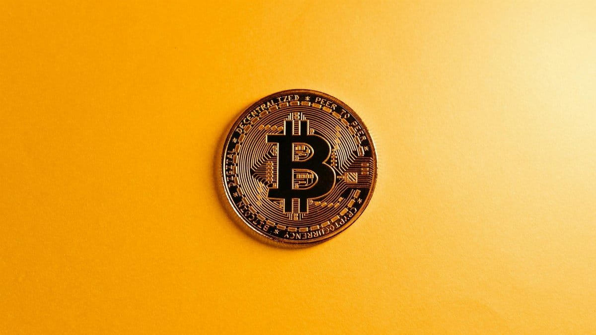 A close-up of a Bitcoin coin on a bright yellow background, symbolizing digital currency.