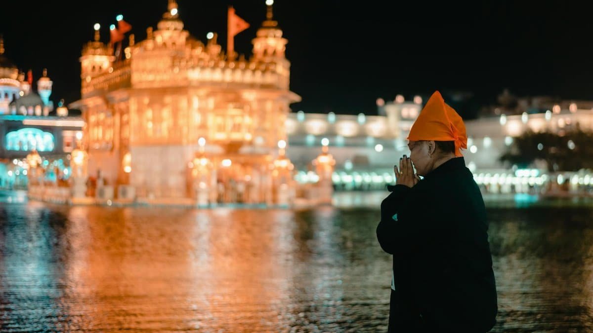 A person prays at the illuminated Golden Temple in Amritsar, a significant Sikh landmark.