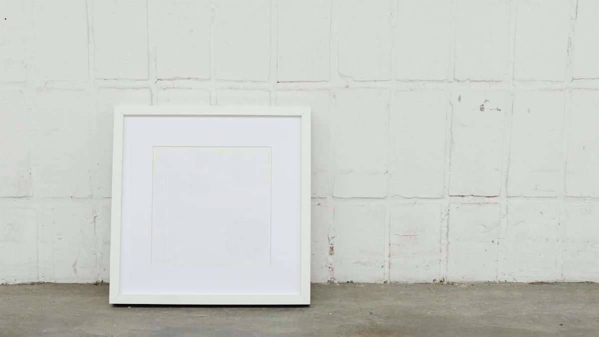 A minimalist white picture frame against a textured concrete wall, offering ample copy space.