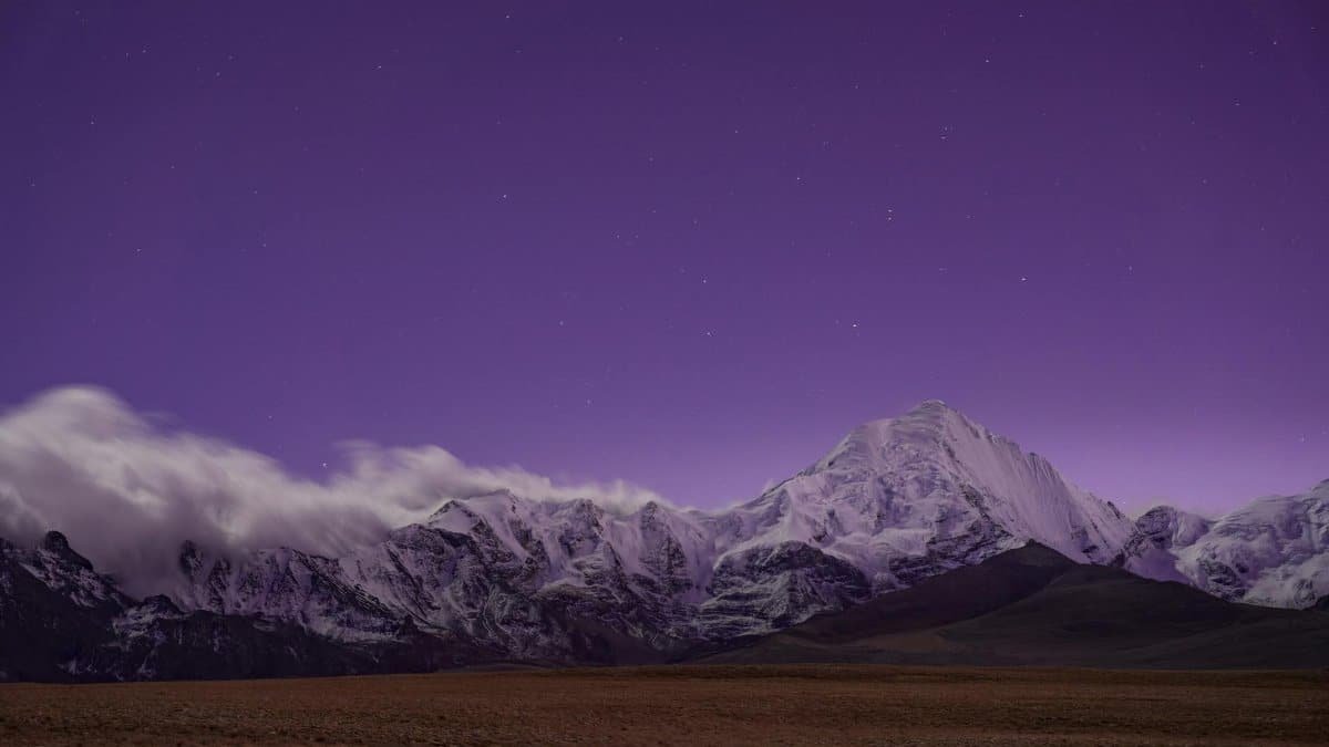 Capture of snowy mountains under a starry purple sky, serene and majestic view.