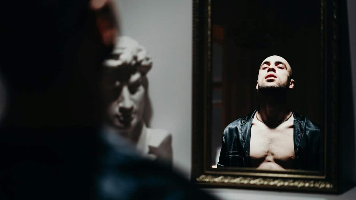 Moody portrait of a man reflecting in a mirror, exploring identity and emotion.