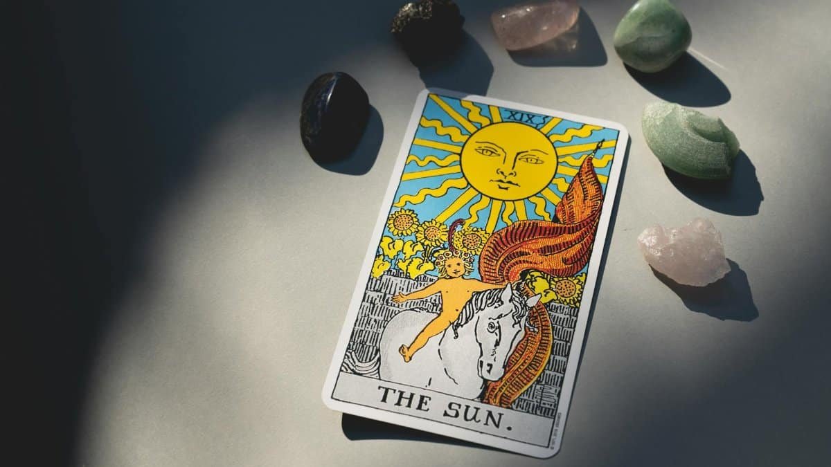 The Sun tarot card and crystals arranged on a surface with dramatic lighting and shadows.