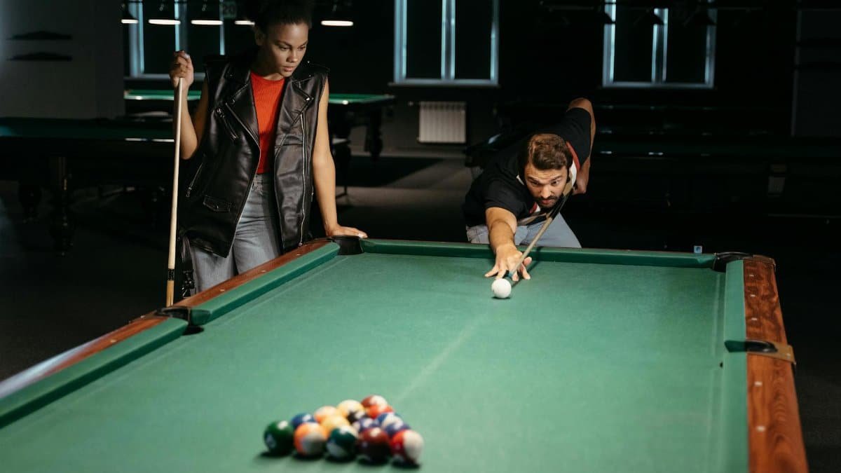 Man and woman playing billiards in an indoor club, aiming for a strategic shot.
