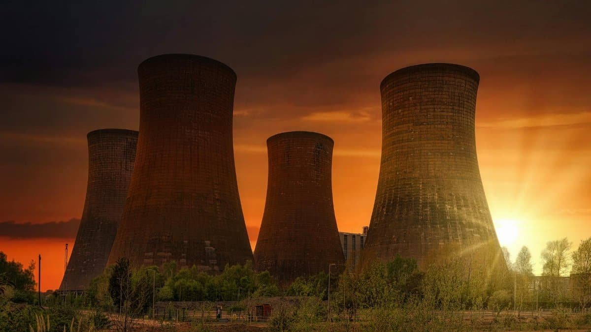 Exterior of huge cooling towers located in contemporary atomic power plant against bright setting sun under dramatic dark sky