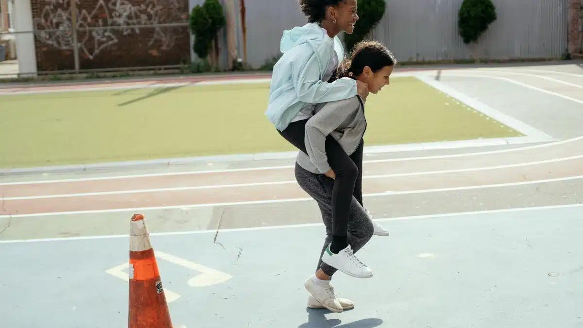 Side view of cheerful diverse teenage girls doing piggyback ride on sports ground during physical education class