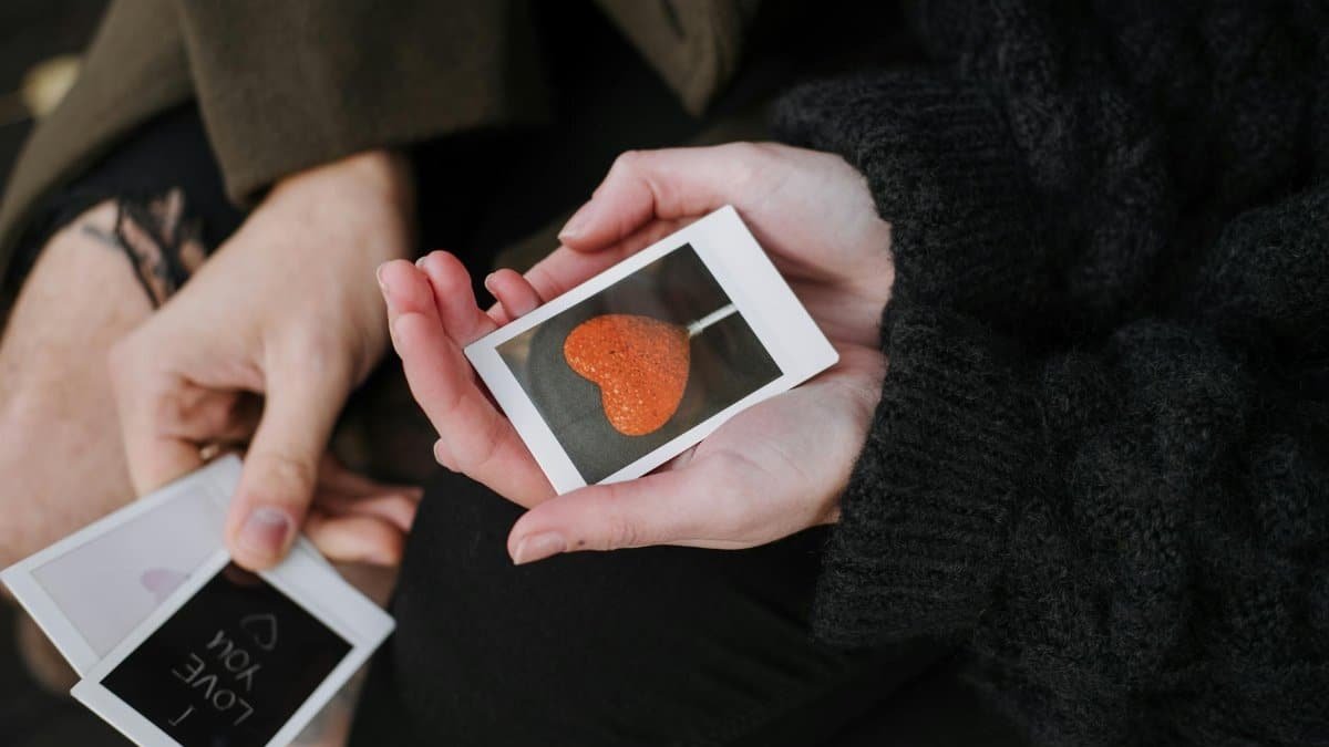 Close-up of hands holding heart-themed polaroids, symbolizing love and connection.
