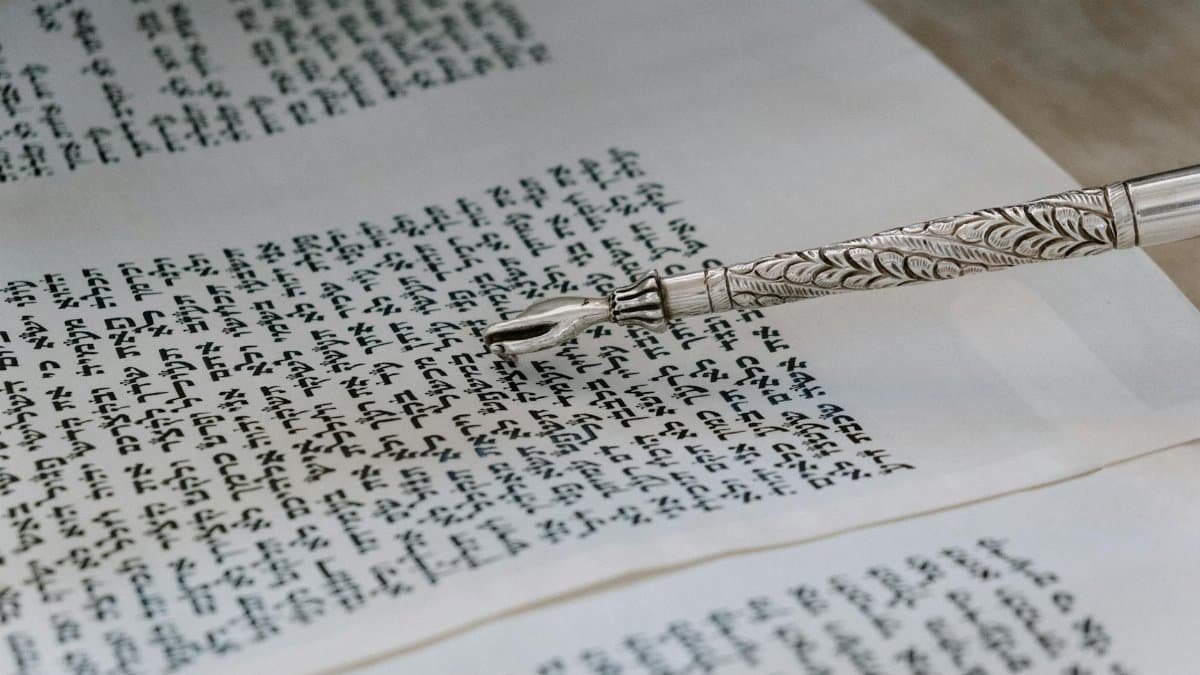 A detailed view of a silver yad pointing to Hebrew text in a Torah scroll.