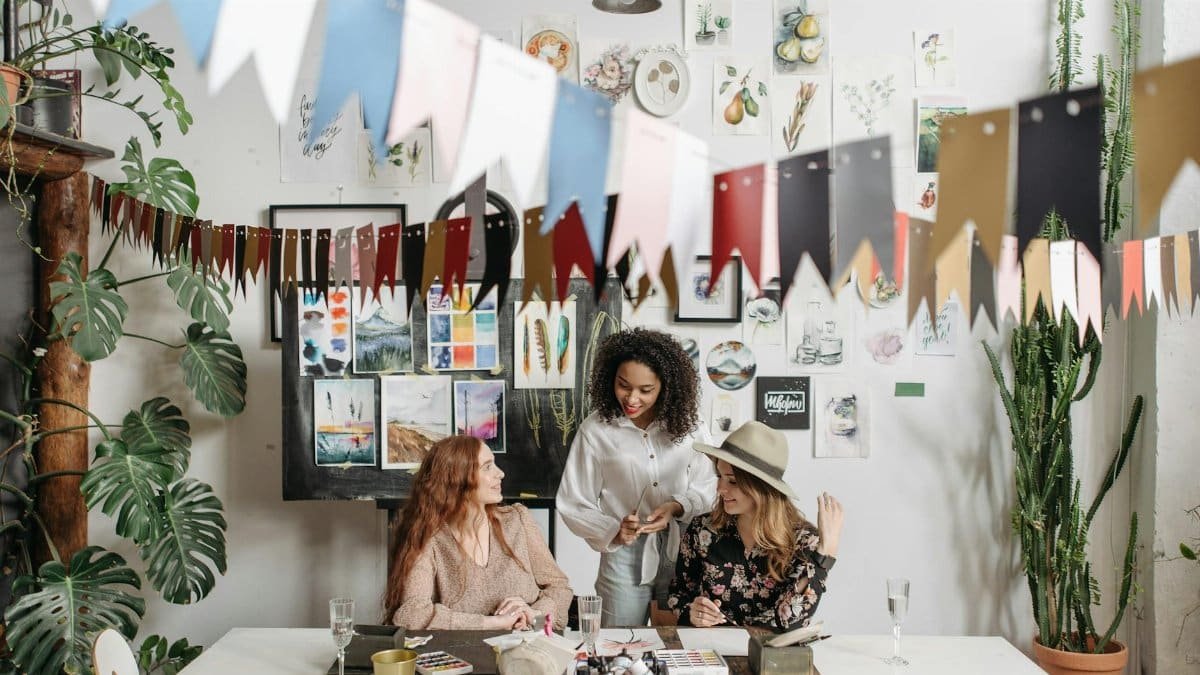 Three women enjoying a creative painting session with colorful decor and plants.