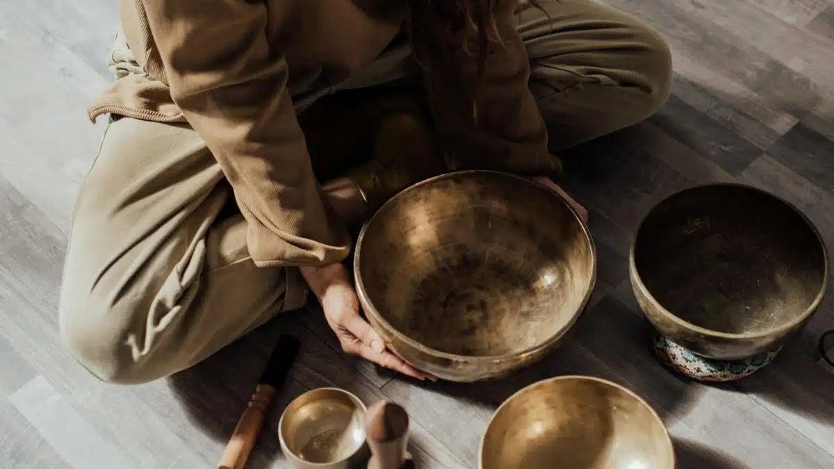 A person meditates with Tibetan singing bowls on a wooden floor, creating a serene atmosphere.