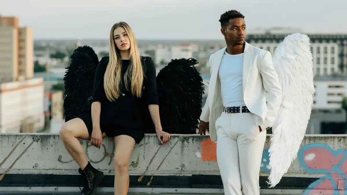 A man and woman dressed as angels on a rooftop, showcasing black and white contrast.