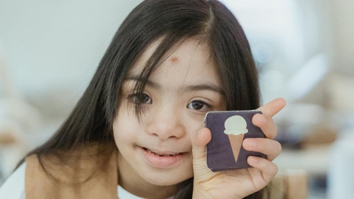 Young girl with Down syndrome smiling and holding a memory game card indoors.