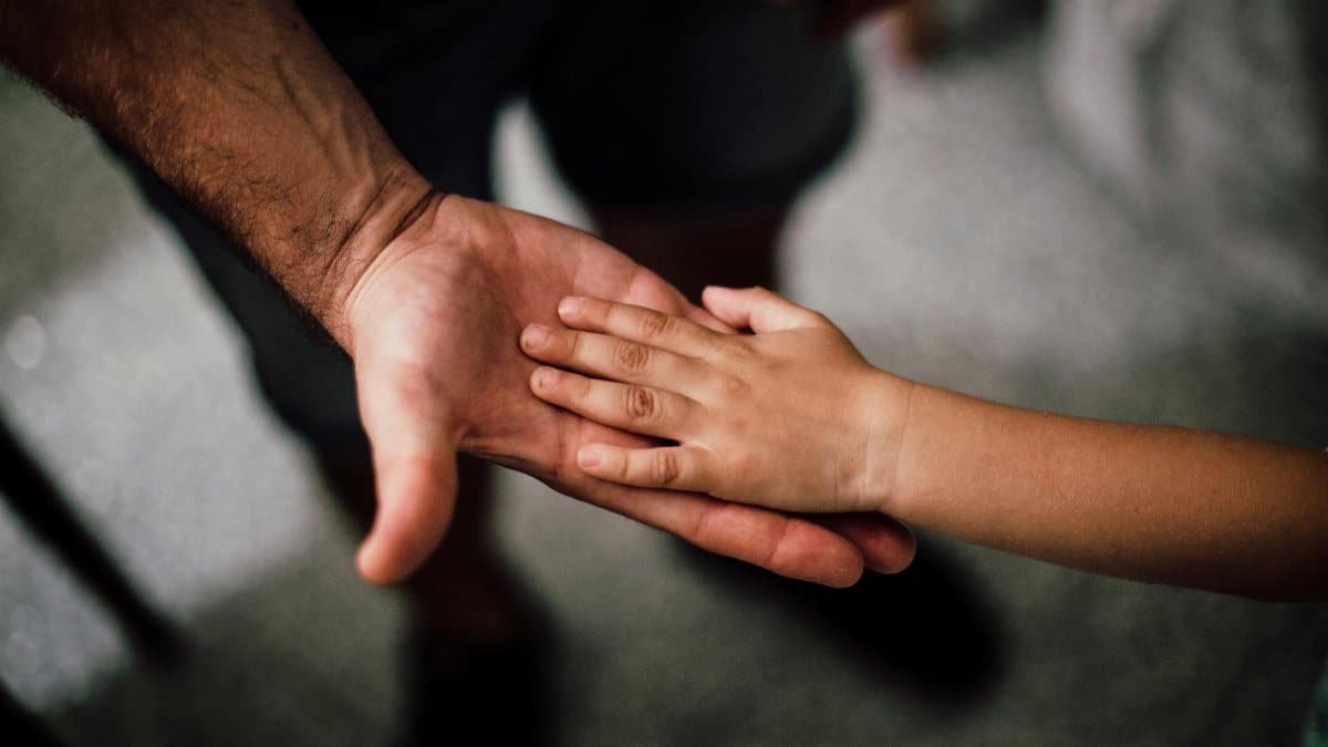 Close-up of a child's hand resting gently on a man's hand, symbolizing love and support.
