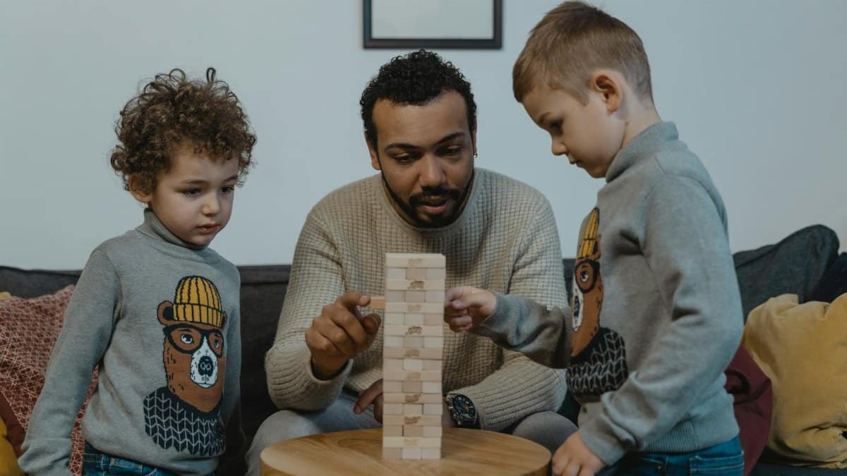 A father and his two sons enjoy a game of Jenga in the living room, highlighting family bonding and fun indoors.