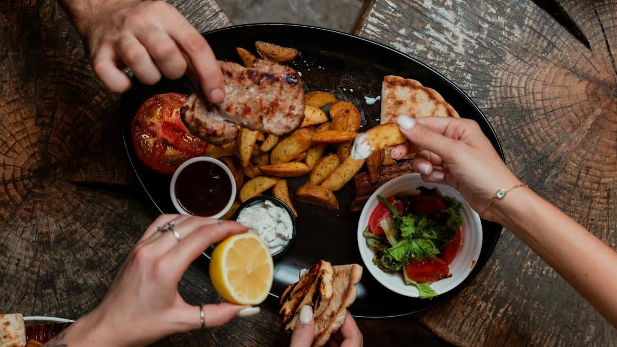 Several people sharing a Mediterranean meal with grilled meats, roasted vegetables, and fresh salad.