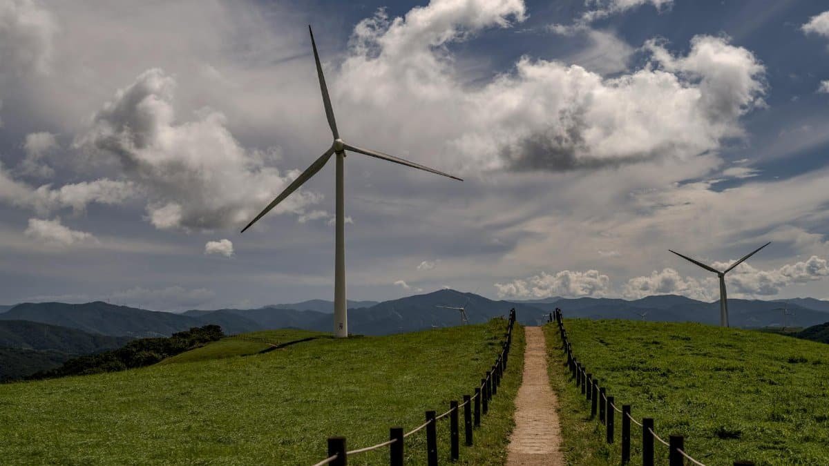 Wind turbines and a dirt path leading through lush hills under a cloudy sky in Korea. Renewable energy concept.