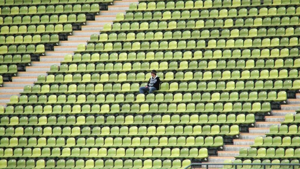A solitary figure sits among green and yellow stadium seats, capturing a moment of solitude in München, Germany.