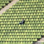 A solitary figure sits among green and yellow stadium seats, capturing a moment of solitude in München, Germany.