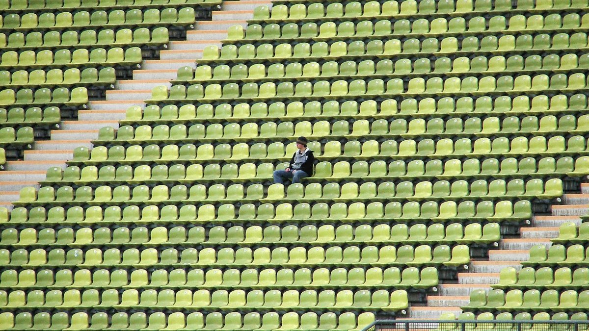 A solitary figure sits among green and yellow stadium seats, capturing a moment of solitude in München, Germany.