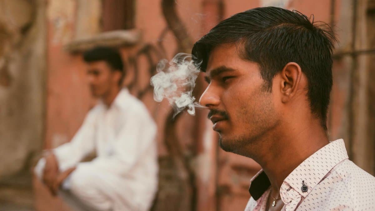 A contemplative young man smokes on a vibrant street in İstanbul, capturing urban life.
