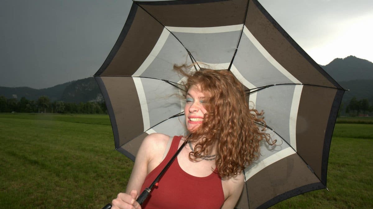 Woman outdoors enjoying a windy day with an umbrella in the countryside.