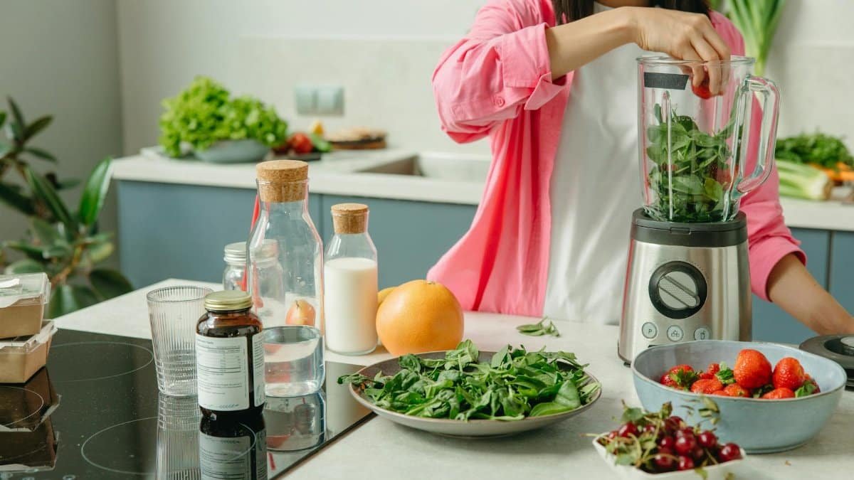 Woman in pink sleeve blending fresh fruits and veggies for a healthy smoothie.