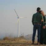 A couple embracing on a hilltop near a wind turbine, showcasing love and renewable energy.