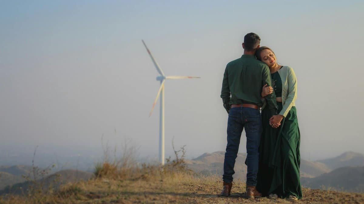 A couple embracing on a hilltop near a wind turbine, showcasing love and renewable energy.