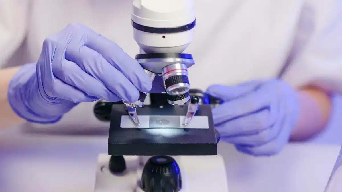 Scientist wearing gloves using a microscope in a laboratory setting.