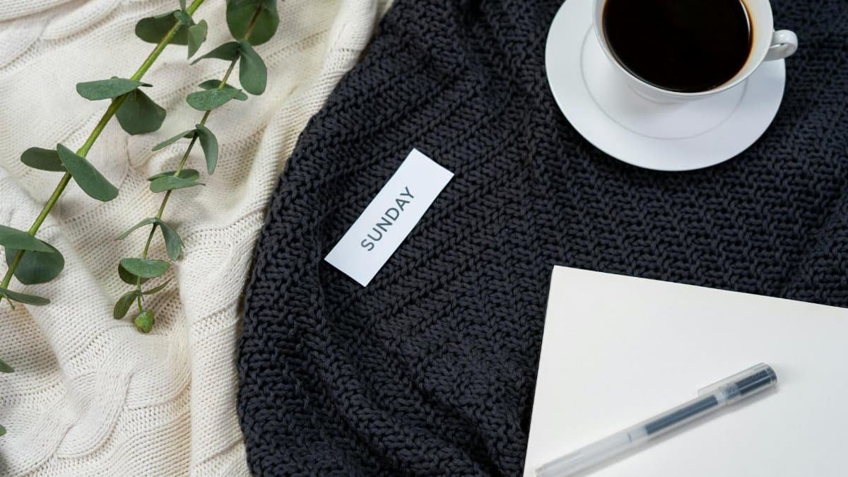 A flat lay of coffee, a knitted blanket, and a notepad creates a cozy Sunday atmosphere.