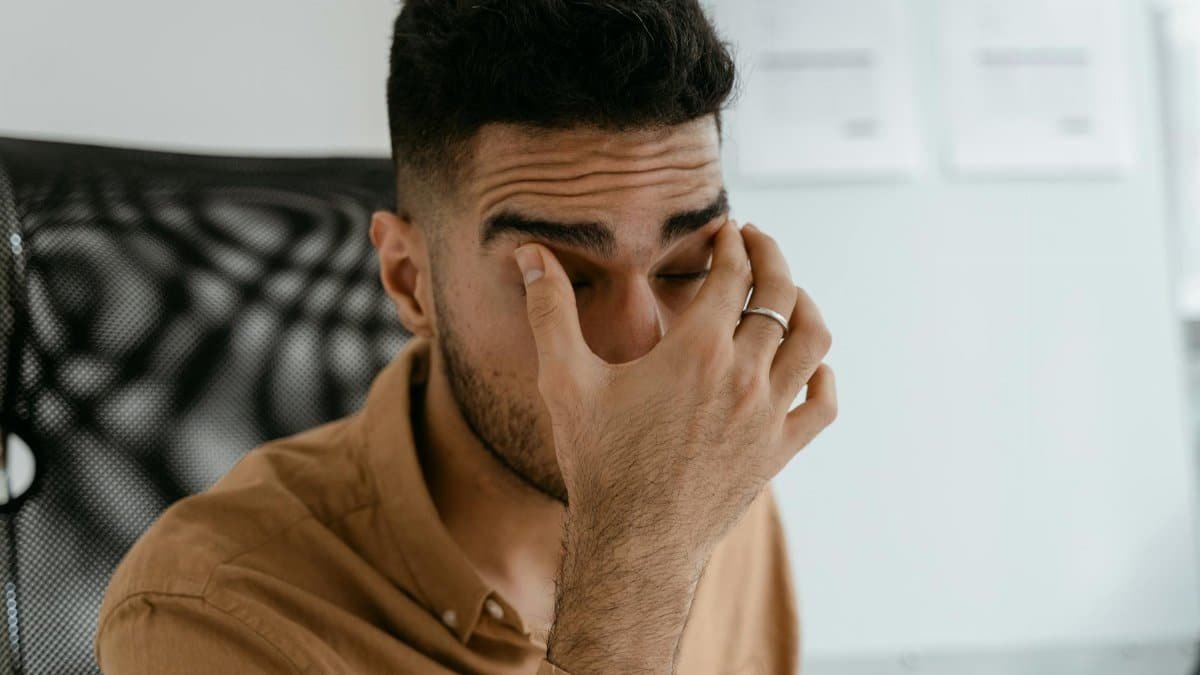 Close-up of a man rubbing his eyes, capturing stress or fatigue in an office environment.
