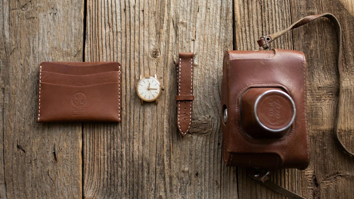 Close-up of leather wallet, watch, and camera case on wooden surface.