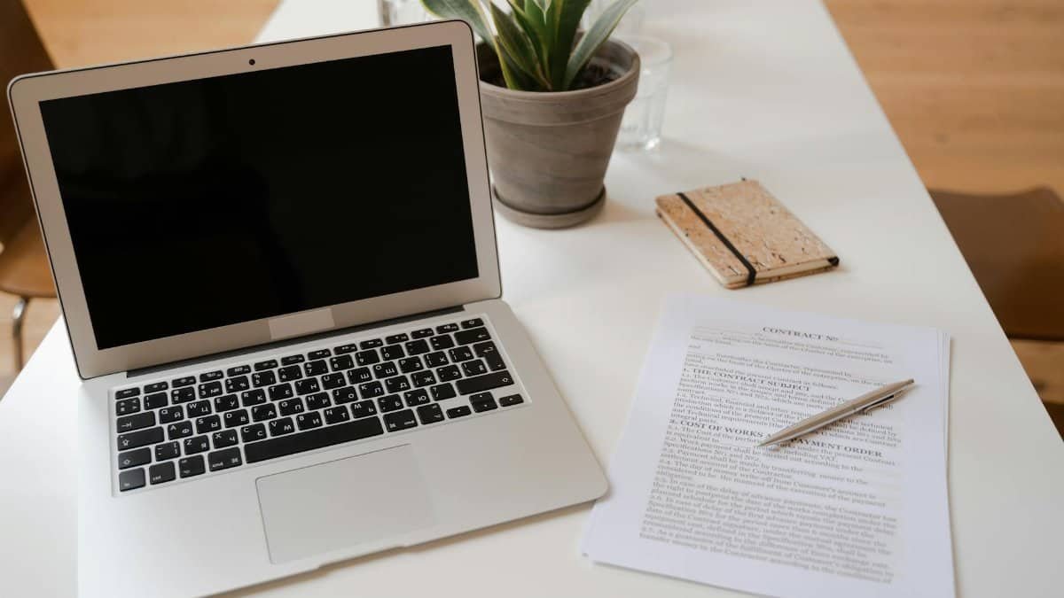 A serene office desk setup featuring a laptop, plant, and contract document ideal for business themes.