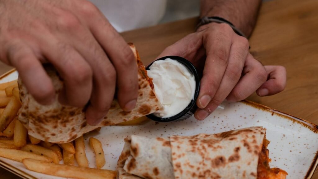Hands dipping a wrap into a sauce with fries on a rustic plate, creating a casual dining scene.