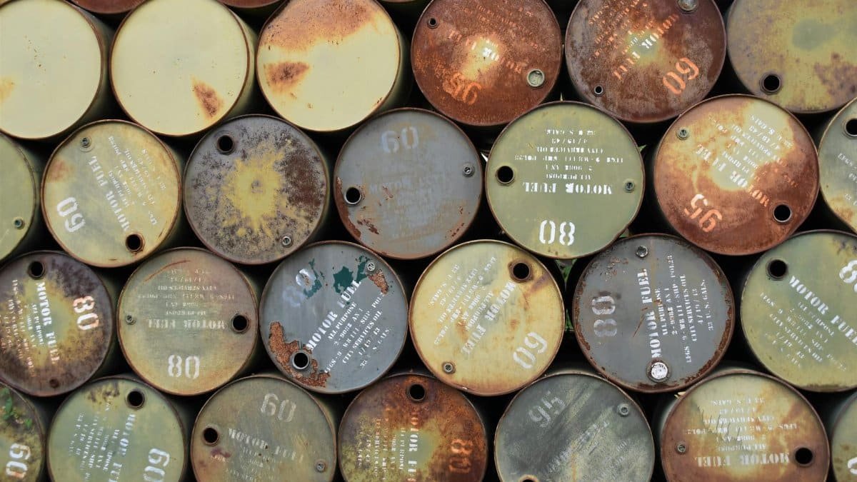 Pile of old, rusty oil barrels stacked outdoors with visible labels and numbers.