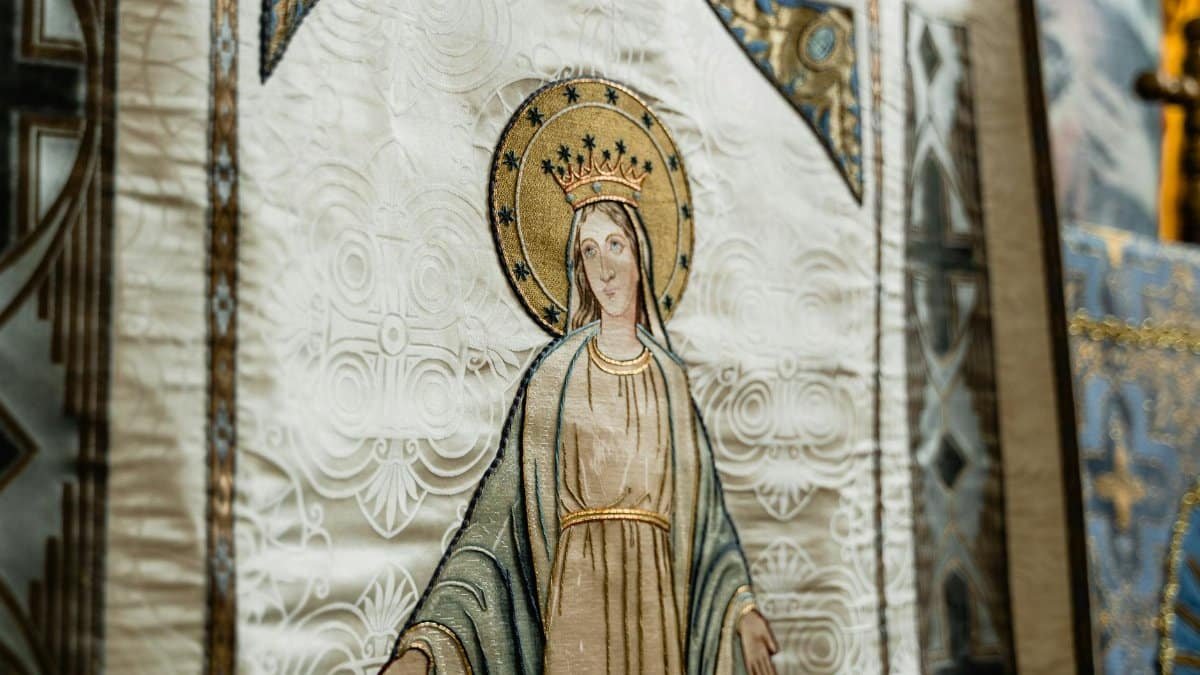 Close-up of a detailed religious tapestry depicting a holy figure with a halo and crown in a cathedral setting.