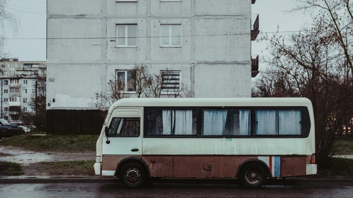 A vintage bus parked on a street in front of a Soviet-era apartment building on a cloudy day.