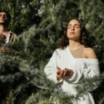 Two adults meditate peacefully amidst lush green trees in a forest.
