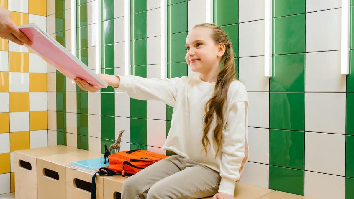 Young girl inside colorful room receiving a notebook with a bright smile.