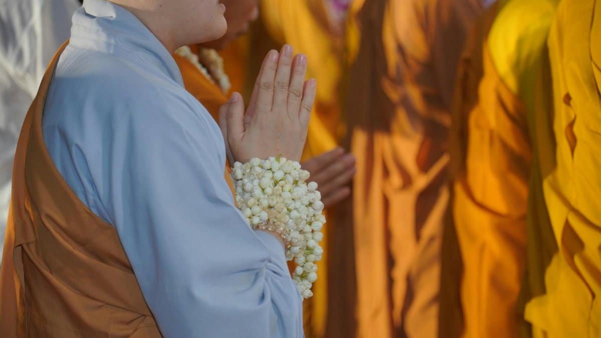 A group of monks dressed in traditional robes participate in a solemn outdoor prayer ceremony.