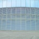 Contemporary glass building wall with aluminum solar facade shading panels on clear sunny day