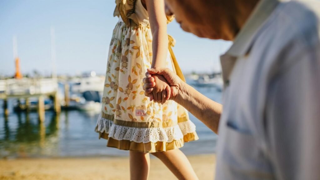 A touching scene of a grandfather holding his granddaughter's hand by the seaside on a sunny day.