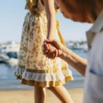 A touching scene of a grandfather holding his granddaughter's hand by the seaside on a sunny day.