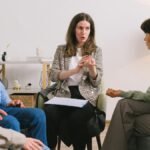 Female therapist during group session talking to female patients gathering in light cozy office