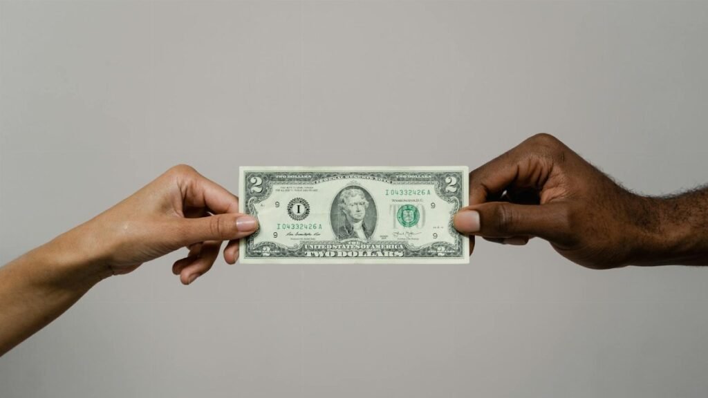 Two hands exchanging a two dollar bill, symbolizing financial transaction.