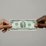 Two hands exchanging a two dollar bill, symbolizing financial transaction.