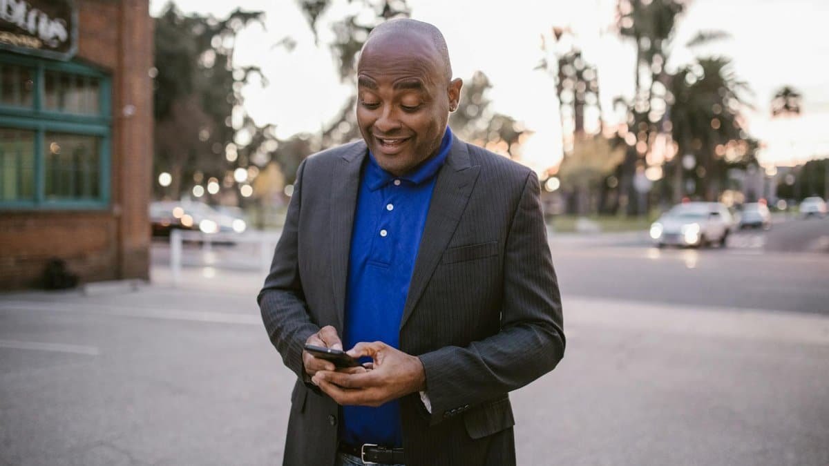 An adult man in a suit is happily using his smartphone outside during sunset, showcasing communication and modern lifestyle.