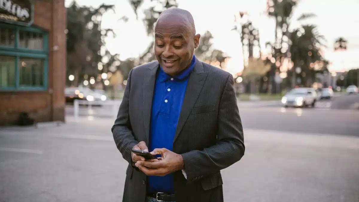 An adult man in a suit is happily using his smartphone outside during sunset, showcasing communication and modern lifestyle.